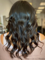 Back view of woman wearing long, curled silk press hair extensions with brown highlights by Melanj Hair.