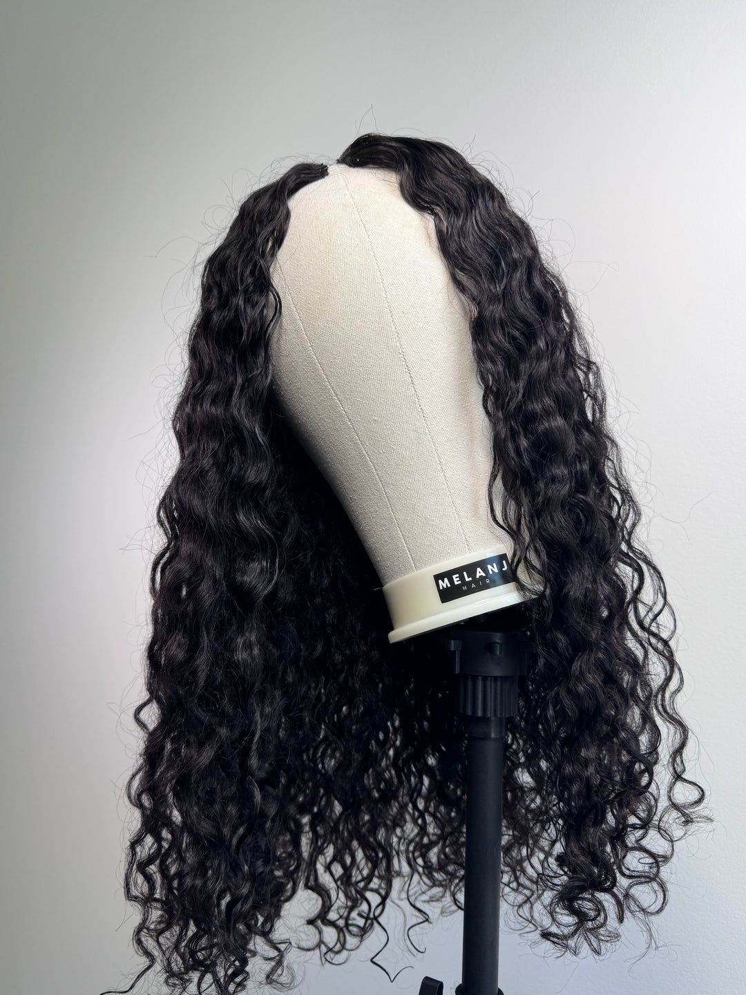 Black wavy curly wig on wig stand by Melanj hair