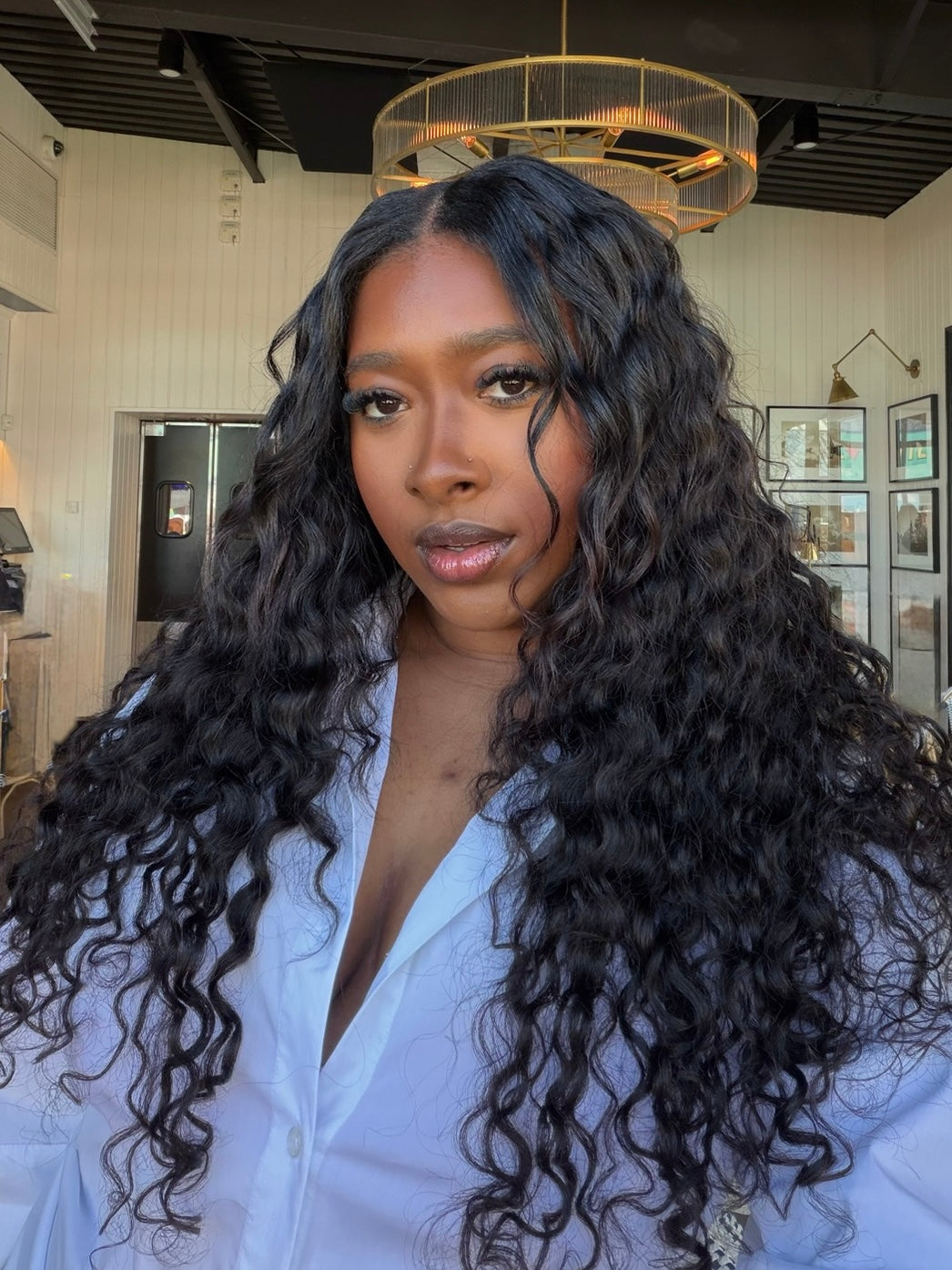 Woman with long, curly hair wearing a white shirt in an indoor setting.